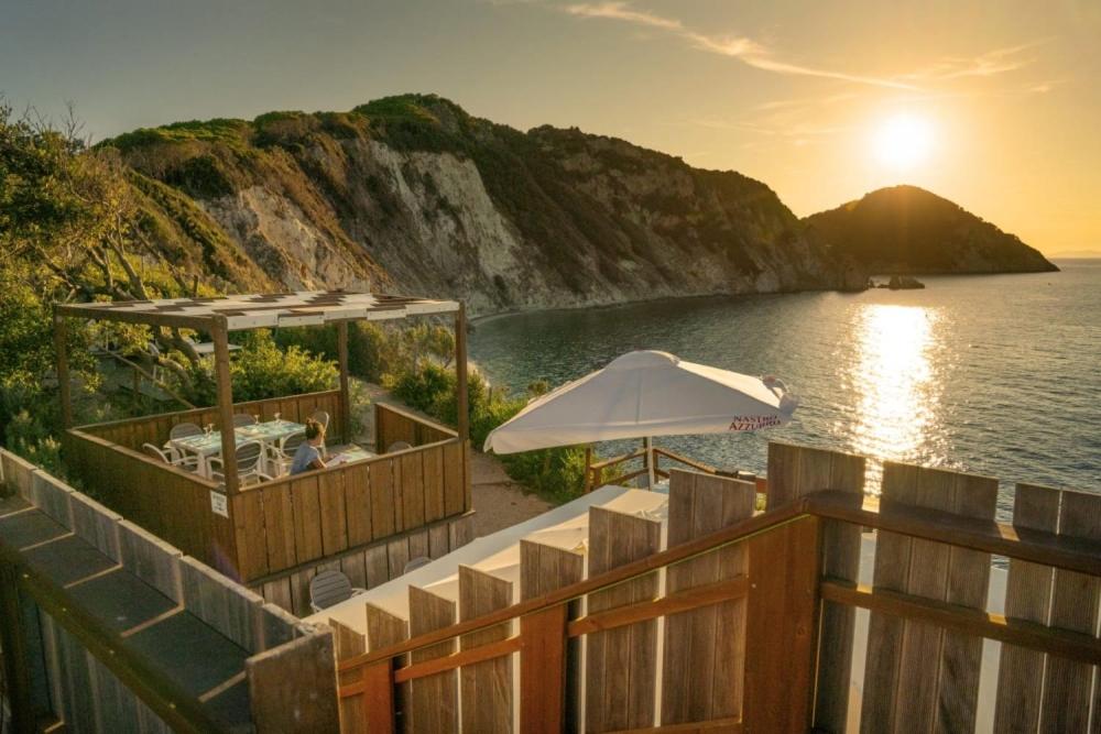 un restaurante con sombrilla y el océano al atardecer en Camping Village La Sorgente, en Portoferraio