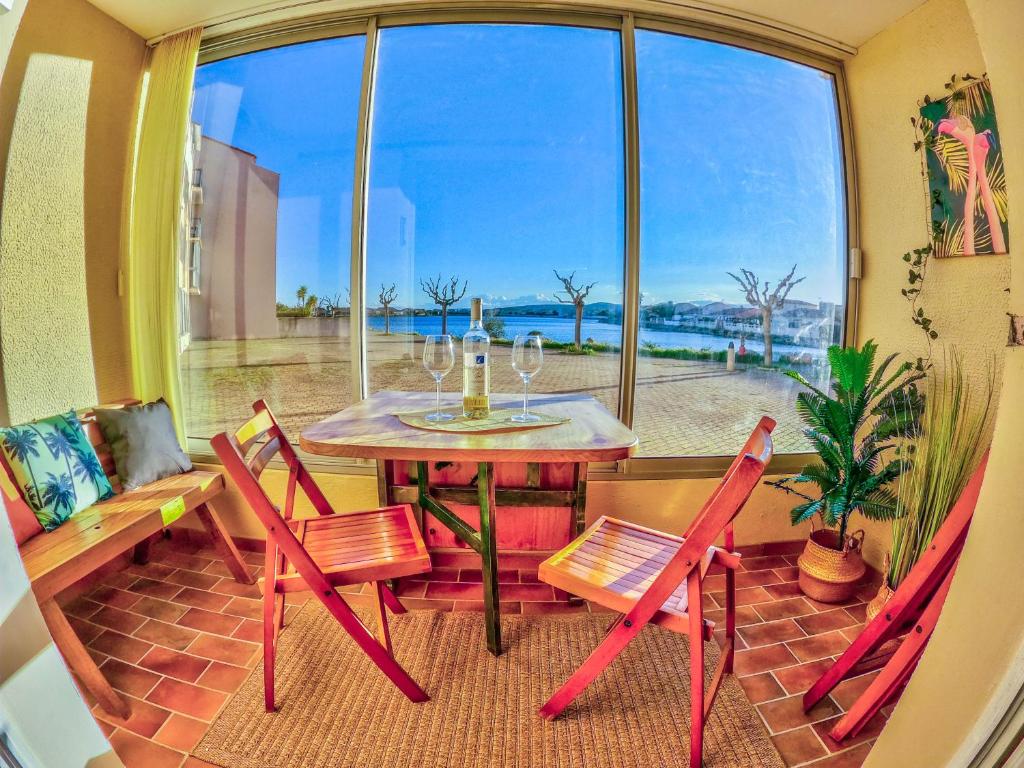 een tafel en stoelen in een kamer met een raam bij Splendide appartement GOLDEN HOUSE vue LAC et montagne in Port-la-Nouvelle