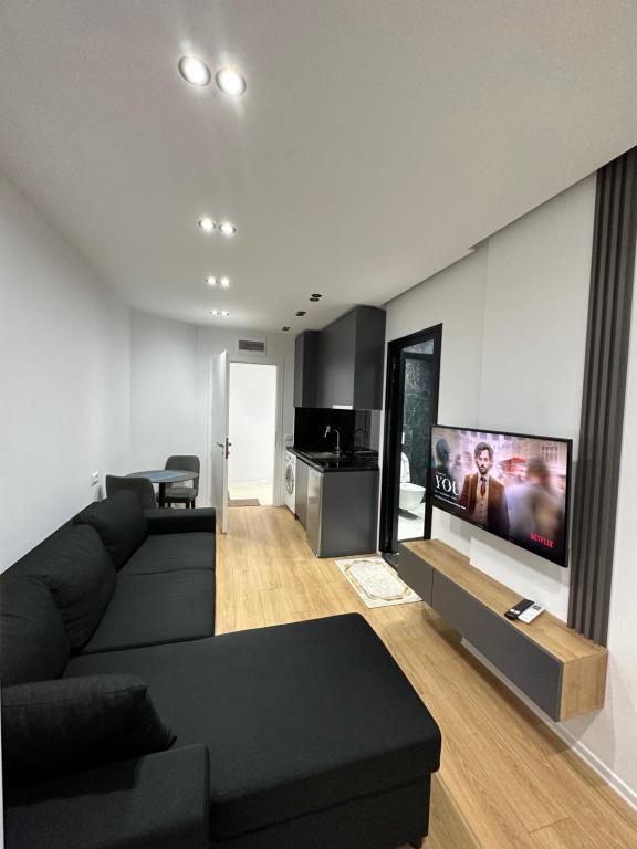 sala de estar con sofá negro y TV de pantalla plana en CozyStayApartments, en Tirana