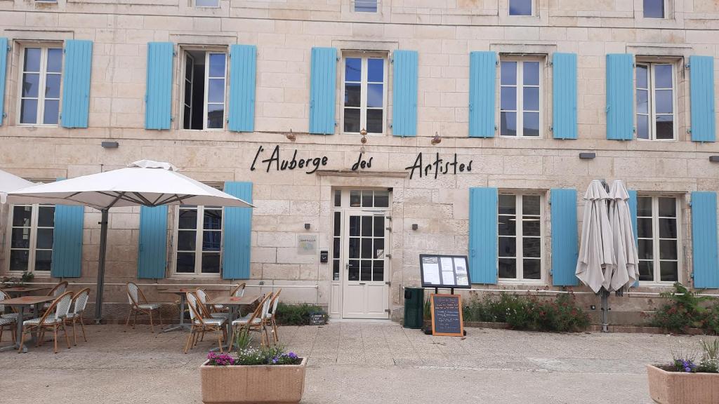 un edificio con puertas azules, mesas y sombrillas en L'Auberge des Artistes, en Nieul-sur-lʼAutise