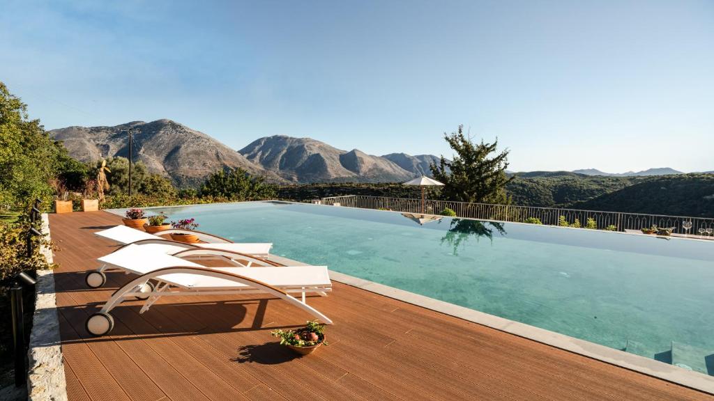 a swimming pool with chairs and mountains in the background at Nassibe Estate in Áyios Ioánnis