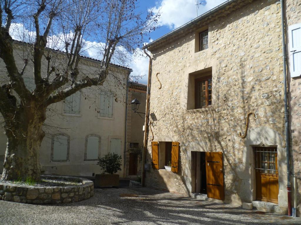 un viejo edificio de piedra con un árbol al lado en Une maison dans le village, en Ribiers