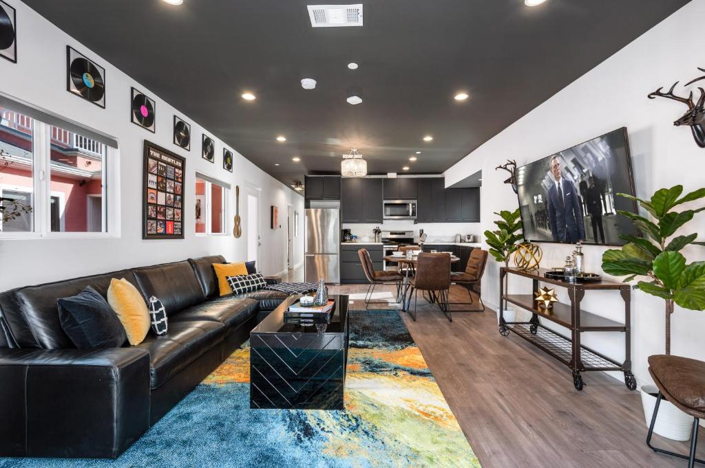 a living room with a black leather couch and a kitchen at Luxe Rock Bungalow in the Heart of Hollywood in Los Angeles