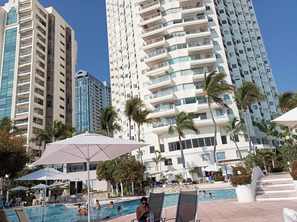 a man sitting in a chair next to a swimming pool with buildings at Ocean Pacific appartment in Acapulco