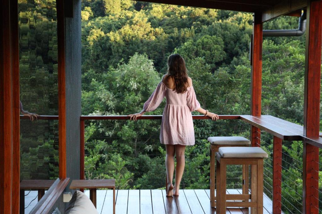 uma mulher de pé numa varanda com vista para a floresta em Waterfall Lodge em Carool