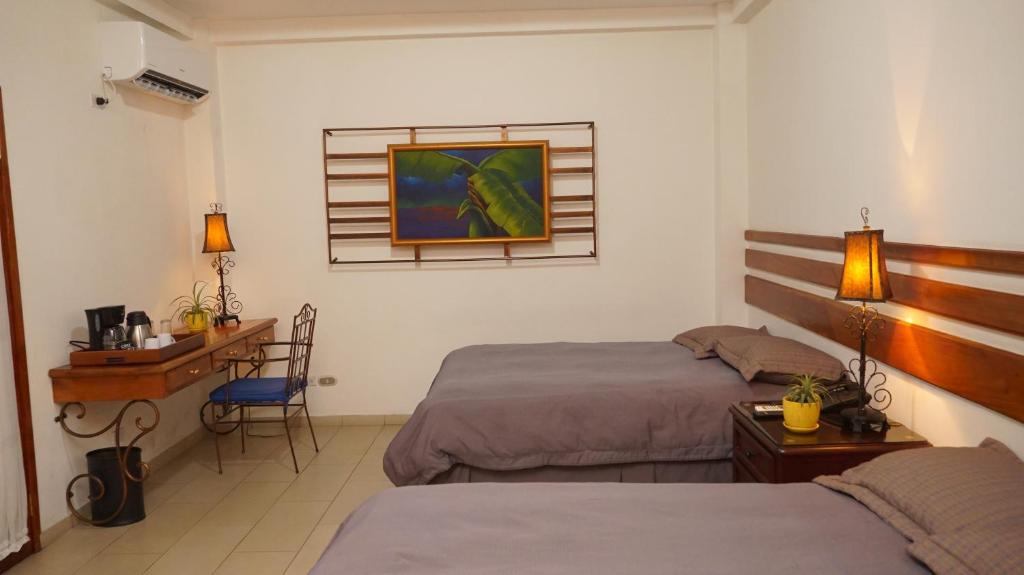 a bedroom with two beds and a desk and a table at Hotel Casa del Arbol in San Pedro Sula