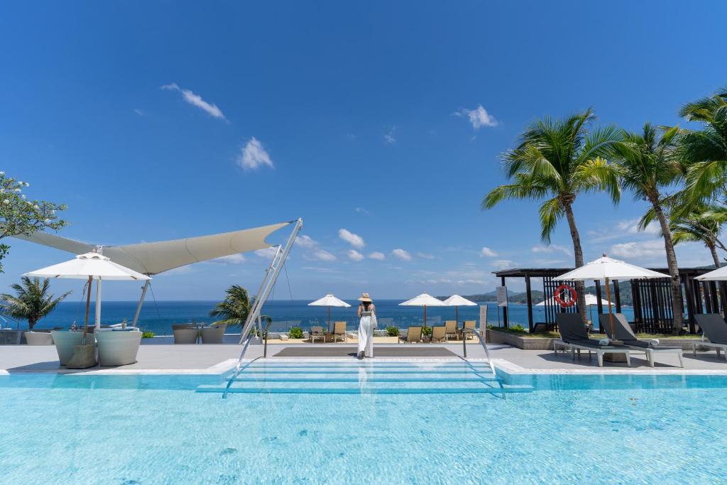 a woman standing next to a swimming pool at a resort at Cape Sienna Phuket Gourmet Hotel & Villas - SHA Extra Plus in Kamala Beach