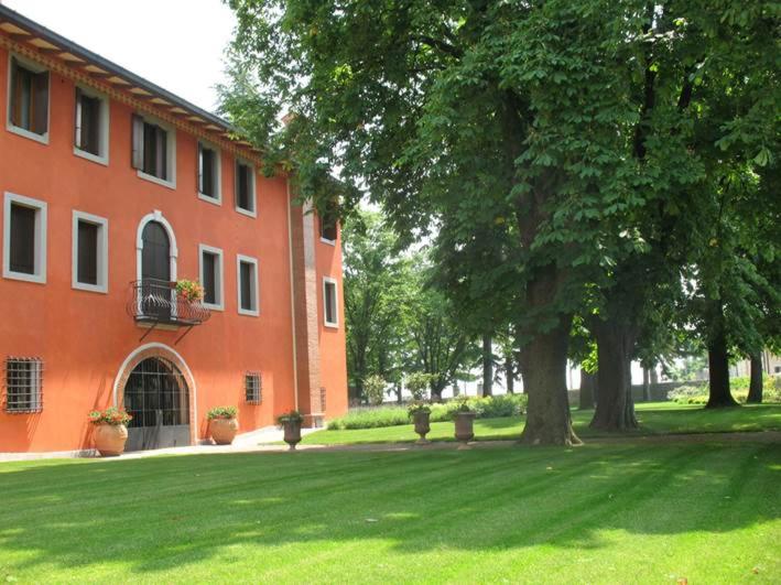 Villa Chiopris في Chiópris-Viscone: مبنى برتقالي به شجرة وساحة عشبية