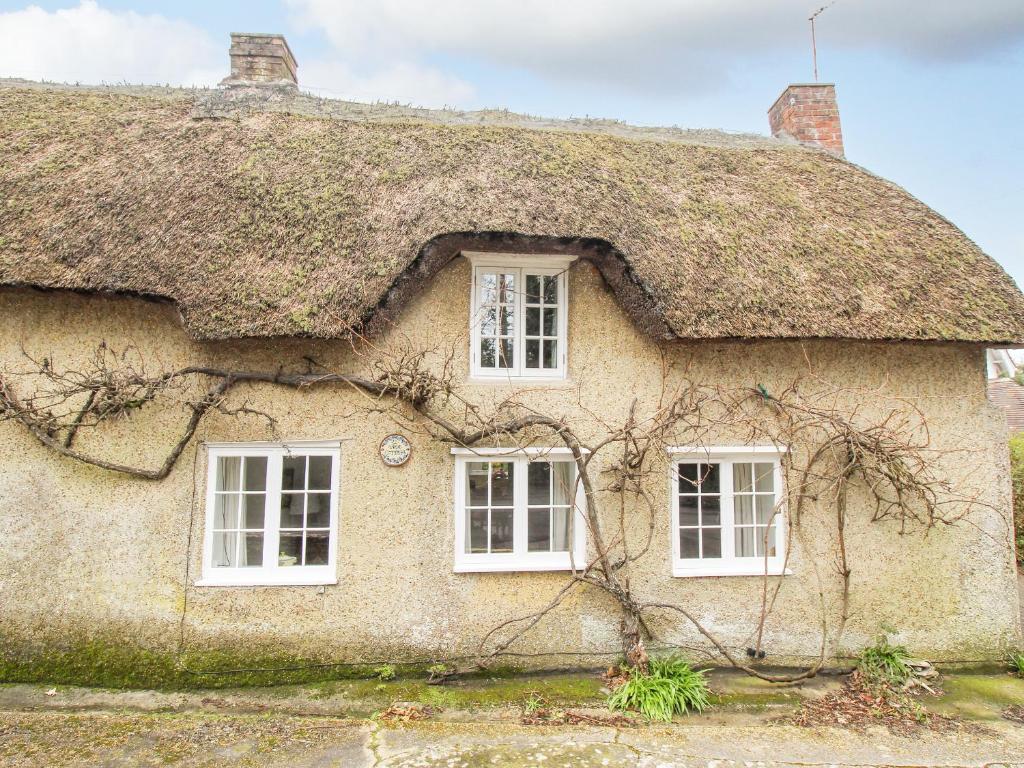 uma casa com telhado de palha e janelas brancas em Vine Cottage em Studland