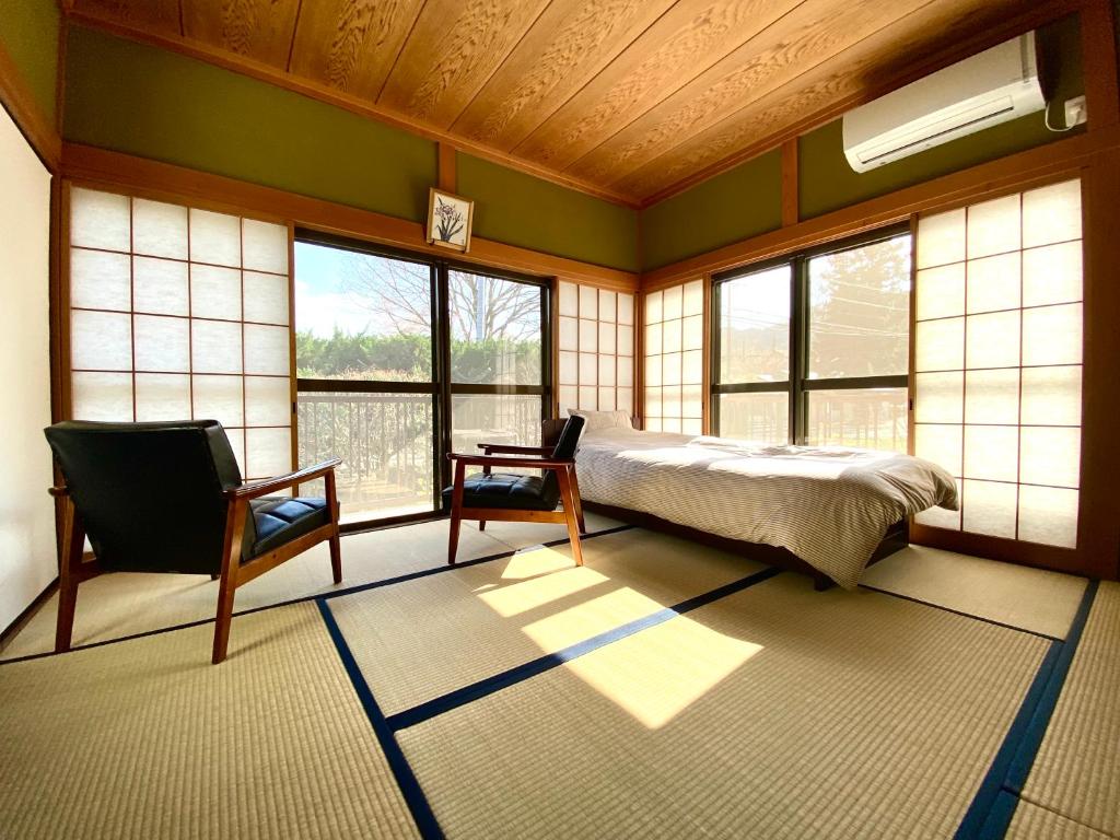 a bedroom with a bed and a chair and windows at Nikko PRIVATE INN WA NODOKA in Nikko