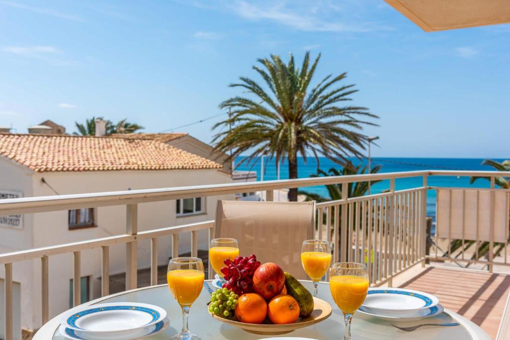 una mesa con un bol de fruta y vasos de zumo de naranja en Apartamento Arenal 7 - PlusHolidays, en Calpe