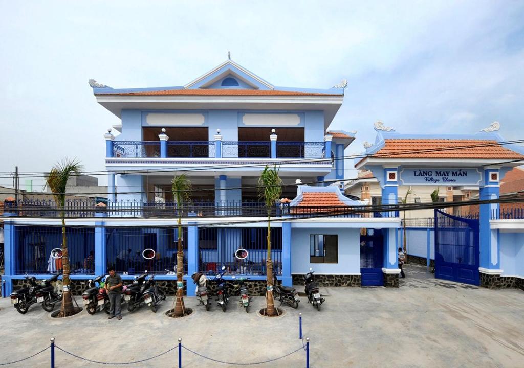 a blue building with palm trees in front of it at Nhà Khách Làng May Mắn - Village Chance in Ho Chi Minh City
