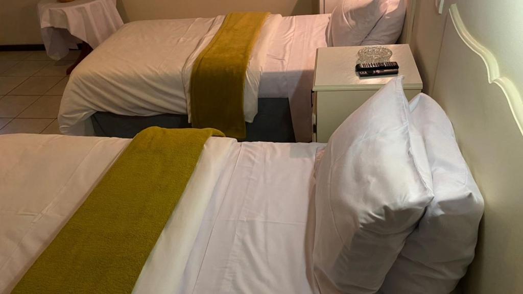 um quarto com 2 camas com lençóis brancos e uma mesa de cabeceira em Twin Room in Hillside - 2087 em Bulawayo
