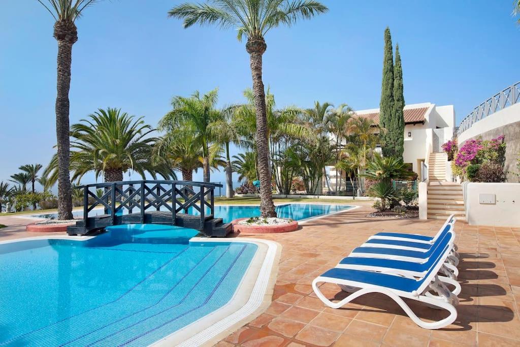 a swimming pool with two lounge chairs and palm trees at Villa Pueblo Don Thomas in San Sebastián de la Gomera