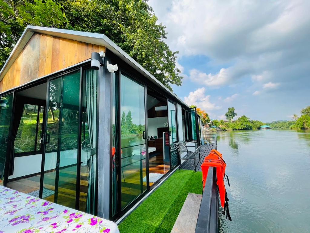 a houseboat on a river with glass windows at เรือนแพคุณมน-Khun Mon Raft in Kanchanaburi City