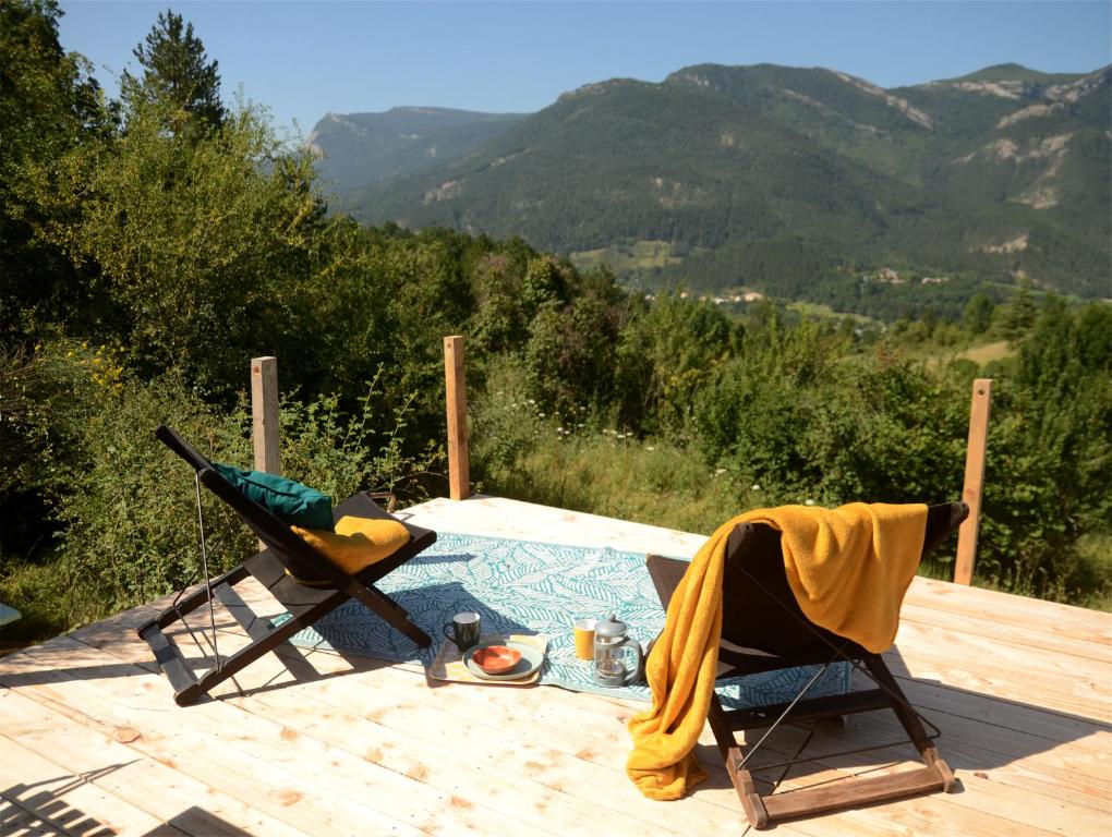 a table and two chairs on a wooden deck with mountains at Ecolodge de la Ferme du Chant de Cailloux in Die