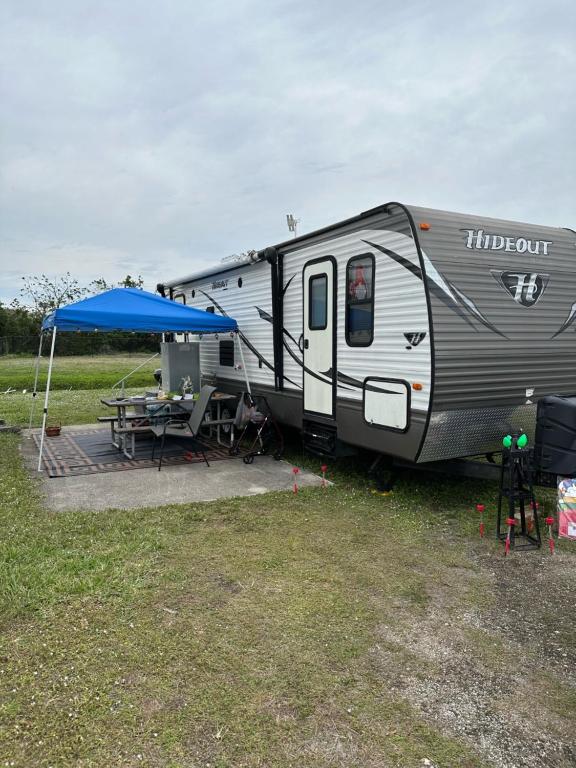 an rv parked in a field with a table and a blue tent at Hideout by Glampers Camp in Port Charlotte
