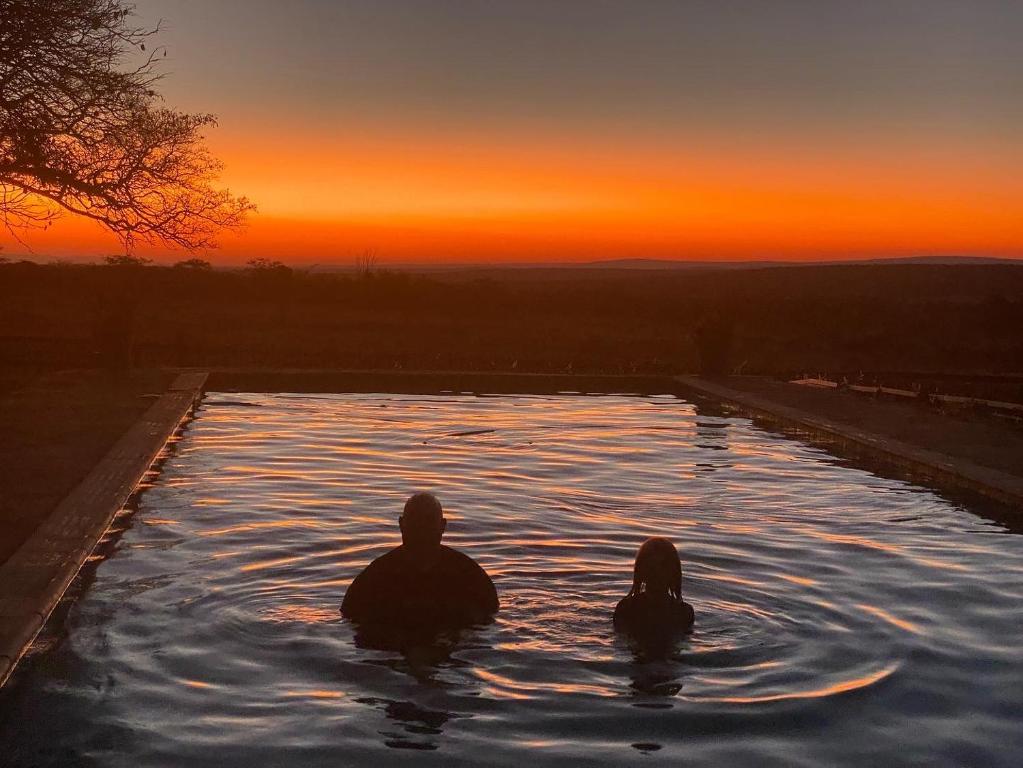 a man and woman sitting in a swimming pool at sunset at Waterberg Cottages, Private Game Reserve in Vaalwater