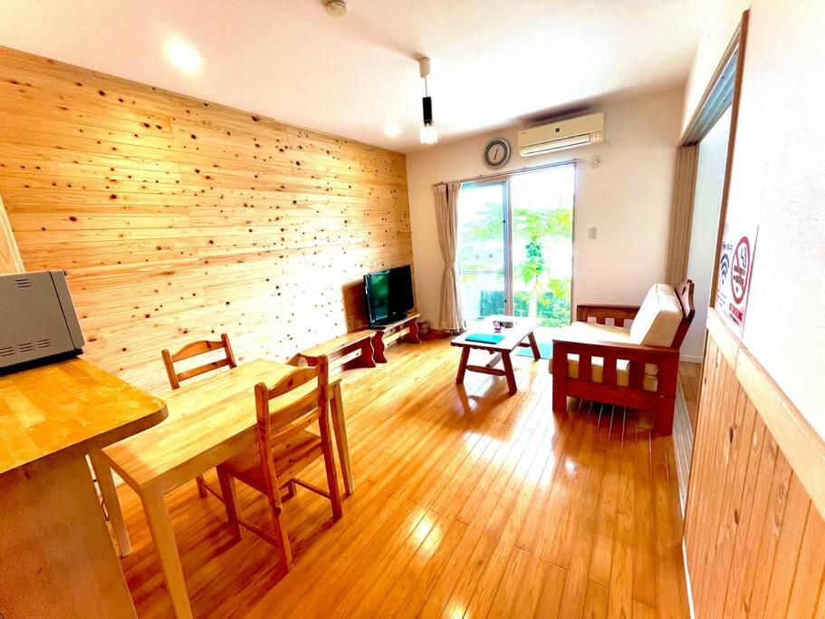 a living room with a wooden wall and a table and chairs at お子様連れ&動物好き大歓迎！産みたての卵を収穫体験できる宿 in Nanjo