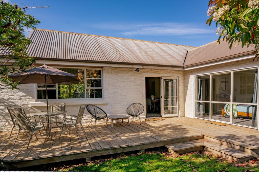 una casa con una terrazza in legno con sedie e ombrellone di Kent Cottage - Arrowtown Holiday Home ad Arrowtown