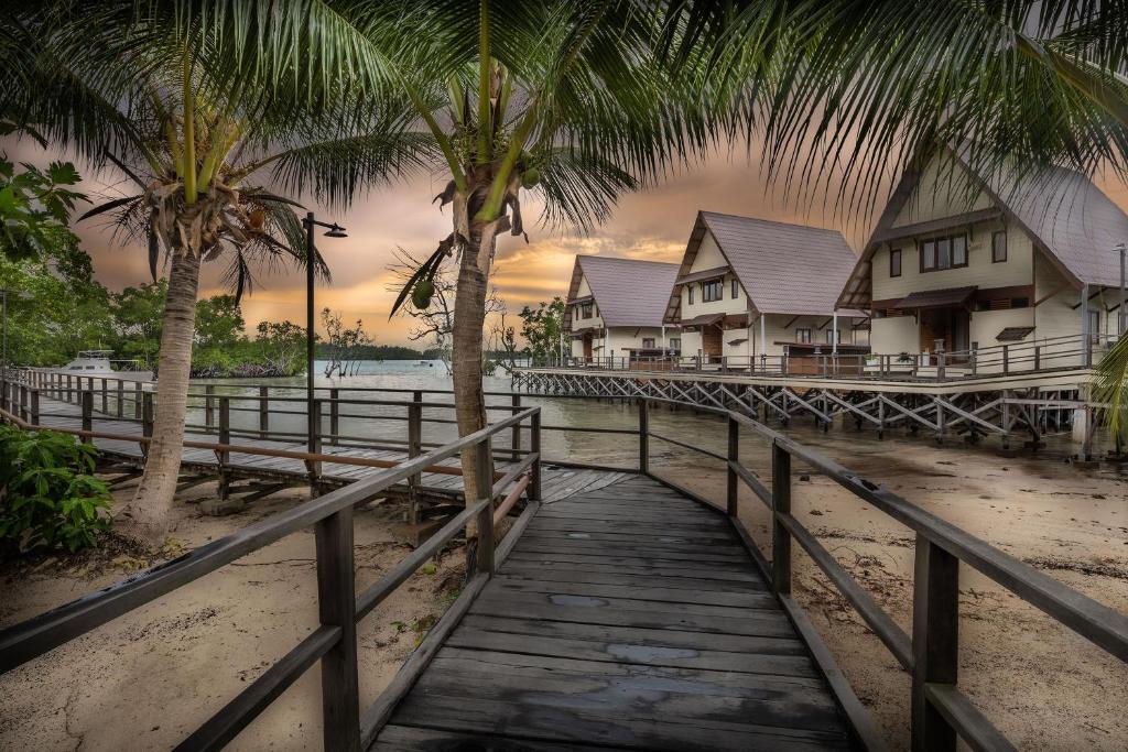 a wooden bridge over a beach with houses and palm trees at Sienna Resort in Maratua Atoll