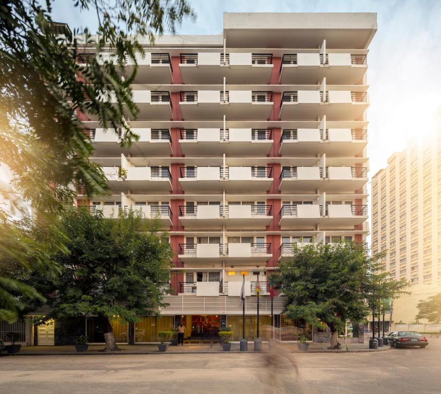 een hoog wit gebouw met bomen ervoor bij Hotel Tivoli Beira in Beira