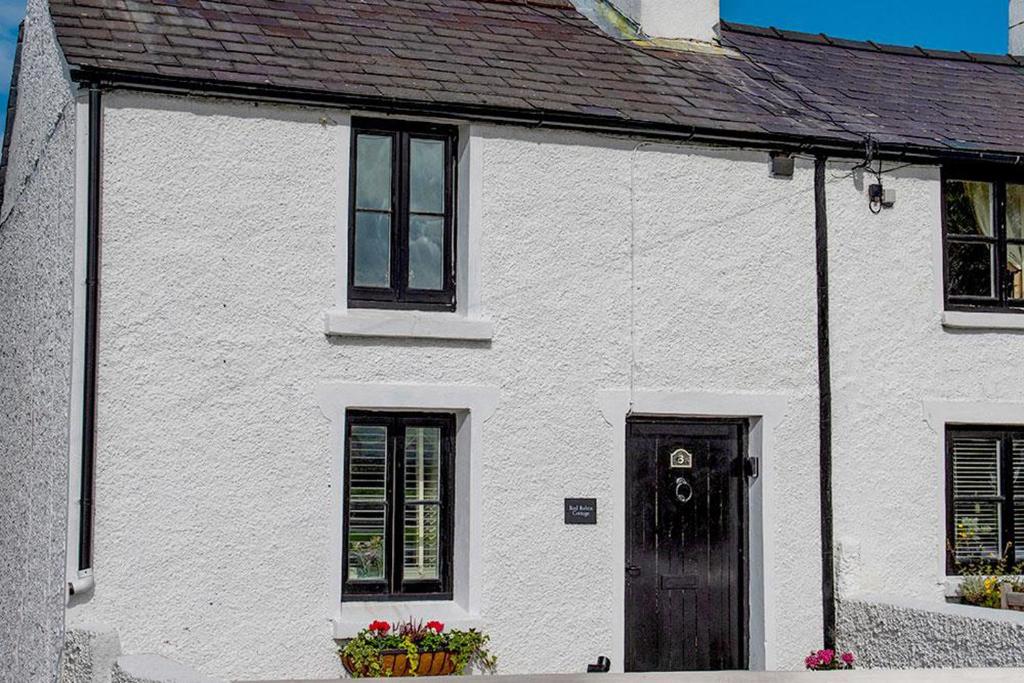 a white house with a black door and windows at Red Robin Cottage in Gaerwen