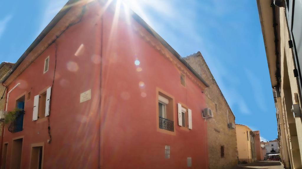 un edificio rojo con el sol brillando en él en ZENSAN Meublé Maison de Village Le Boulou 66160 en Le Boulou