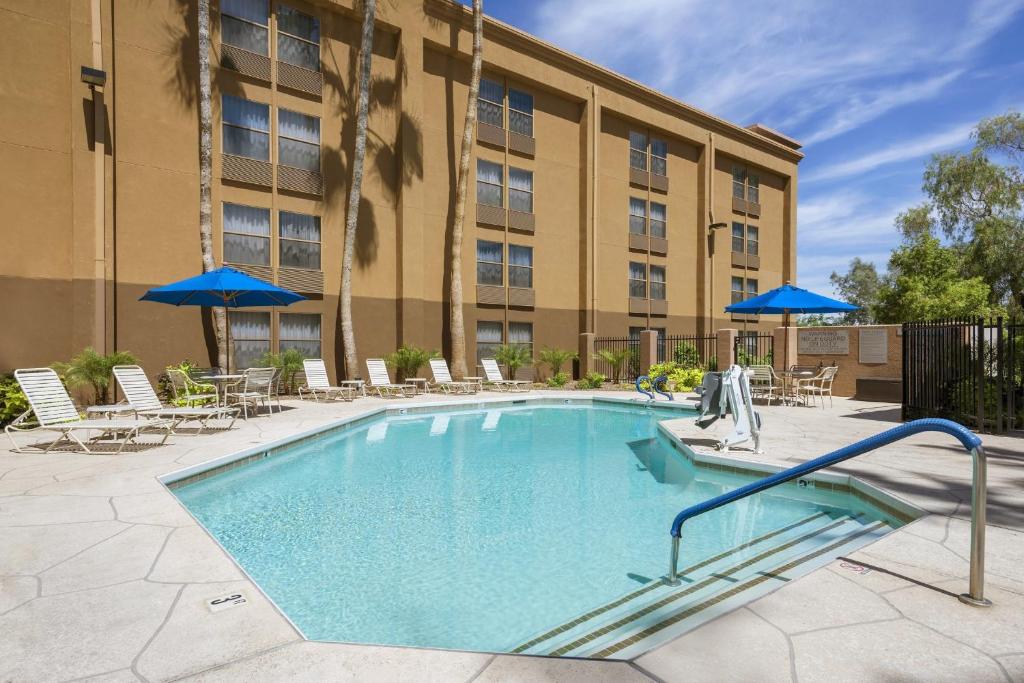 a swimming pool with chairs and umbrellas in front of a building at GreenTree Inn & Suites Phoenix Sky Harbor in Phoenix