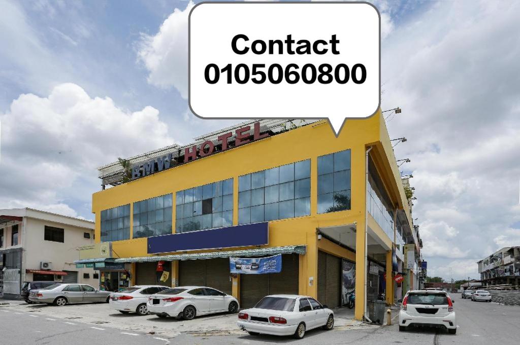 a yellow building with cars parked in a parking lot at BMW Hotel in Muar