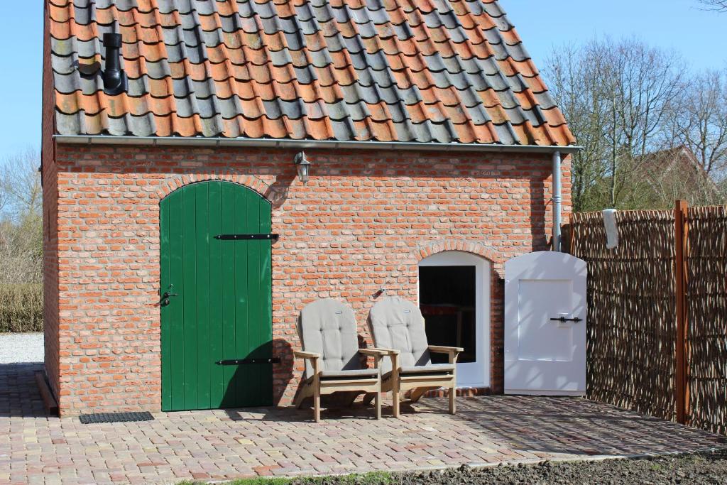 un edificio de ladrillo con 2 sillas y una puerta verde en Trekkershuisje 't Zeeuws Knoopje en Aagtekerke