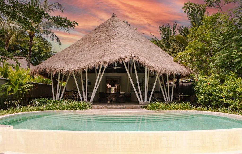 a resort swimming pool with a thatch roof at Beach Villas Lombok in Tanjung