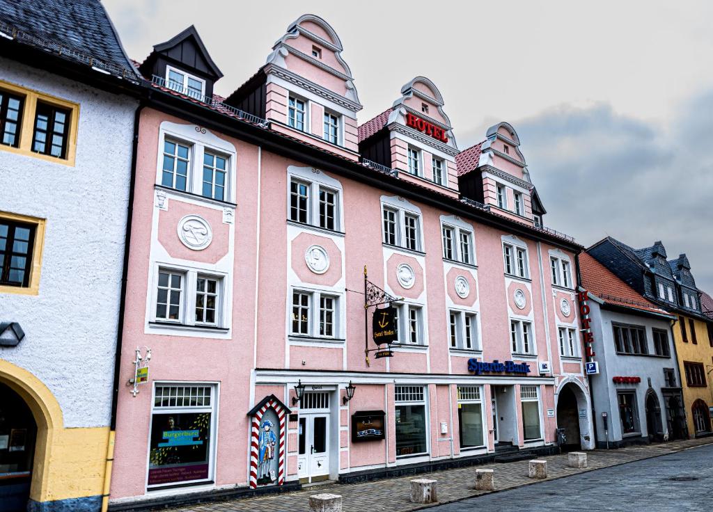 a pink building with clocks on it on a street at Hotel Anker in Saalfeld