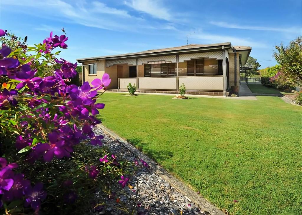 a house with a yard with purple flowers at Rose Cottage in Sawtell