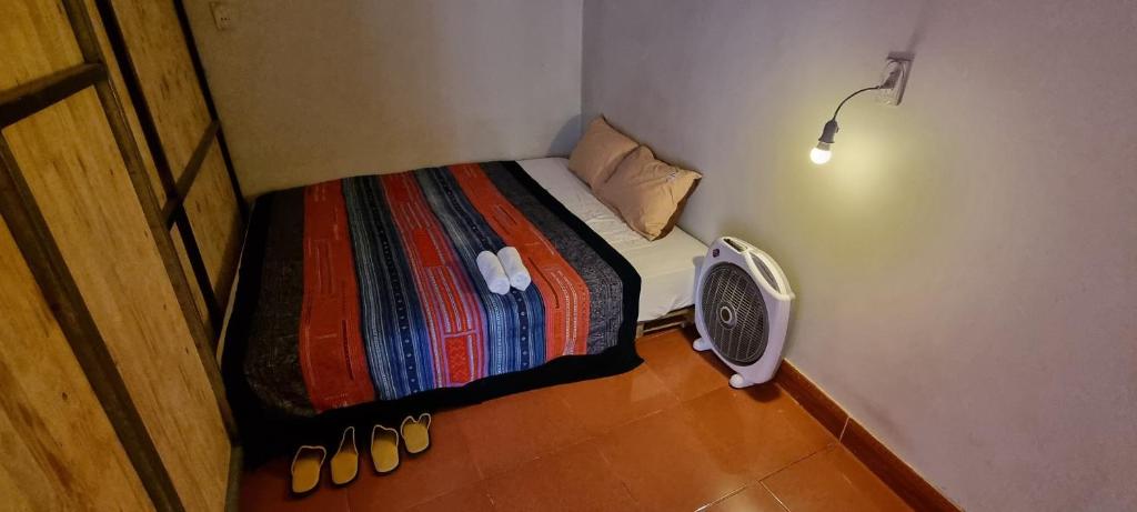 Rainbow House Ha Giang في ها زانغ: غرفة صغيرة بها سرير مع مروحة وأحذية