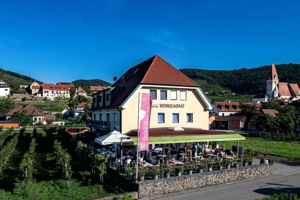 a building with tables and umbrellas in front of it at Hotel Garni Weinquadrat in Weissenkirchen in der Wachau