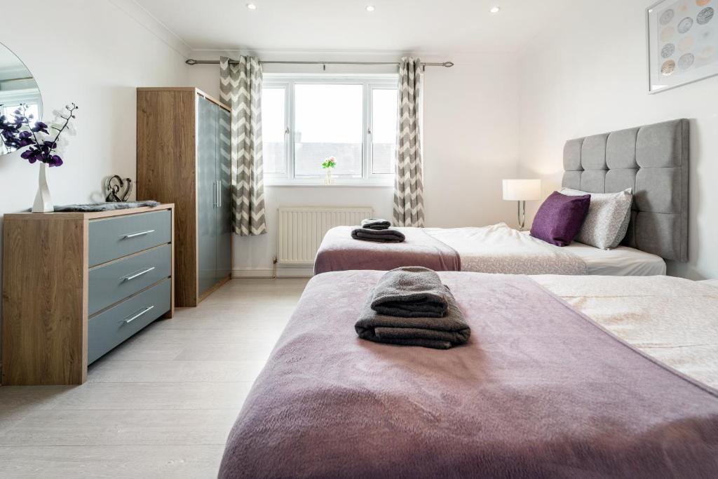 a bedroom with two beds and a dresser with towels at Dwellers Delight Living Ltd Serviced Accommodation, Chigwell, London 3 bedroom House, Upto 7 Guests, Free Wifi & Parking in London