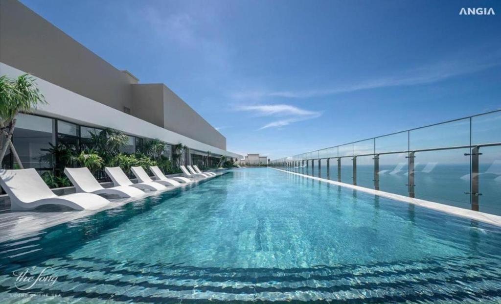 une piscine avec des chaises blanches et l'océan dans l'établissement MeoMeo Homestay - The Sóng Apartment, à Vung Tau