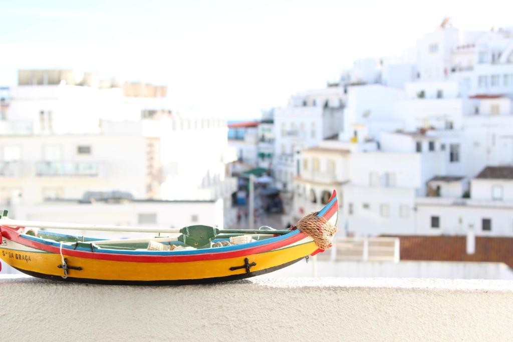 un pequeño barco sentado en el suelo con edificios en el fondo en Rich & Poor Hostel Albufeira, en Albufeira