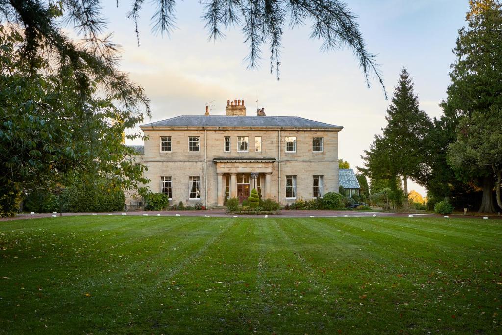 a large white house with a large grass field at Macdonald Linden Hall Hotel, Golf & Spa in Longhorsley