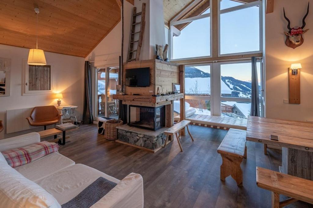 a living room with a fireplace and a large window at L'ourse et L'ange - Luxury chalet (8p). 3 bedrooms, 2 bathrooms and a loft. In the centre of Vallandry, with ski-in & out in Landry
