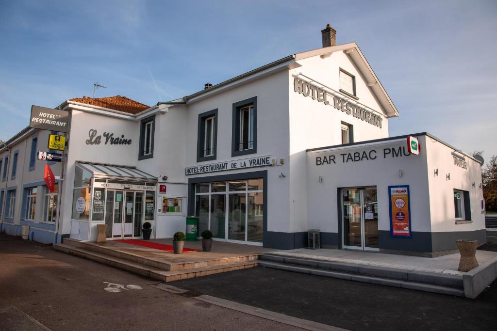 a white building with shops on a street at Logis Hôtel Restaurant La Vraine in Gironcourt-sur-Vraine