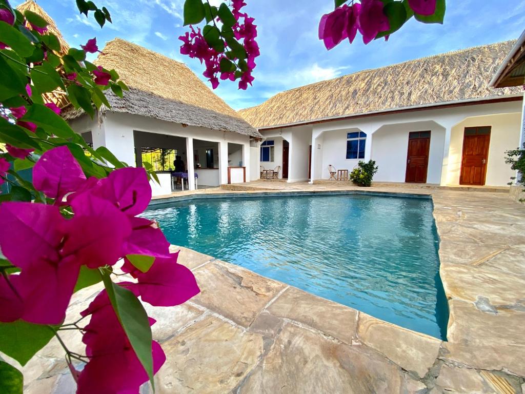 una piscina en el patio trasero de una casa con flores púrpuras en Dragonfly, en Jambiani