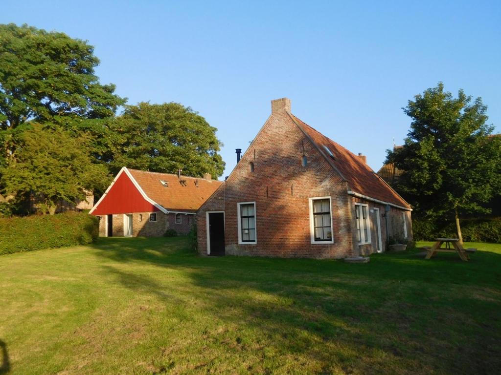 an old brick house with a red roof on a field at Logementen Jannum in Birdaard