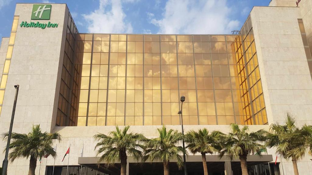 a building with palm trees in front of it at Holiday Inn Kuwait Al Thuraya City by IHG in Kuwait
