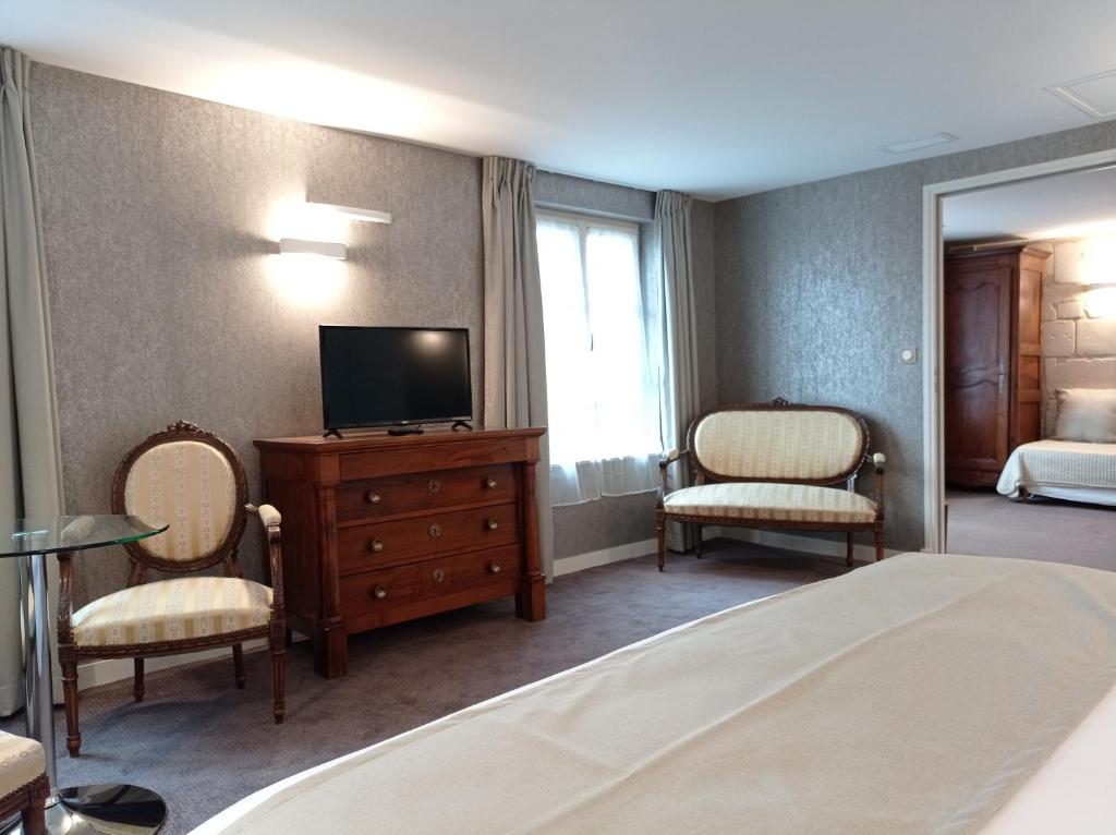 a hotel room with a bed and a tv and two chairs at Hôtel Grand Monarque in Azay-le-Rideau