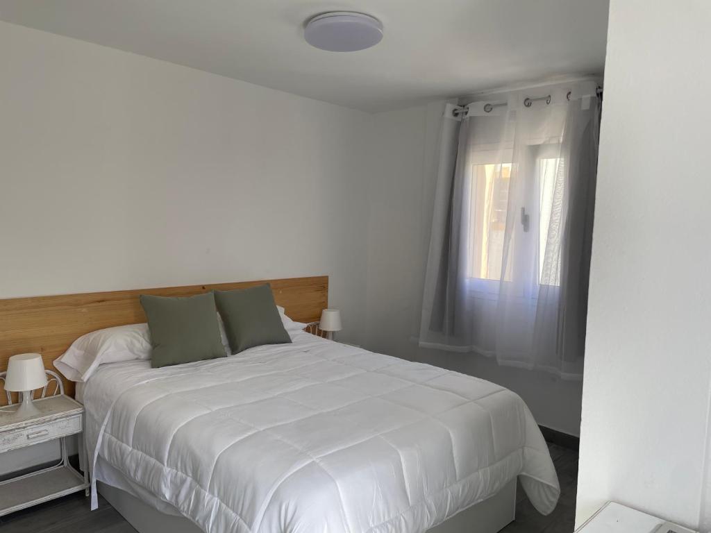 una camera bianca con un grande letto bianco e una finestra di Apartamento Ilusión a Corralejo