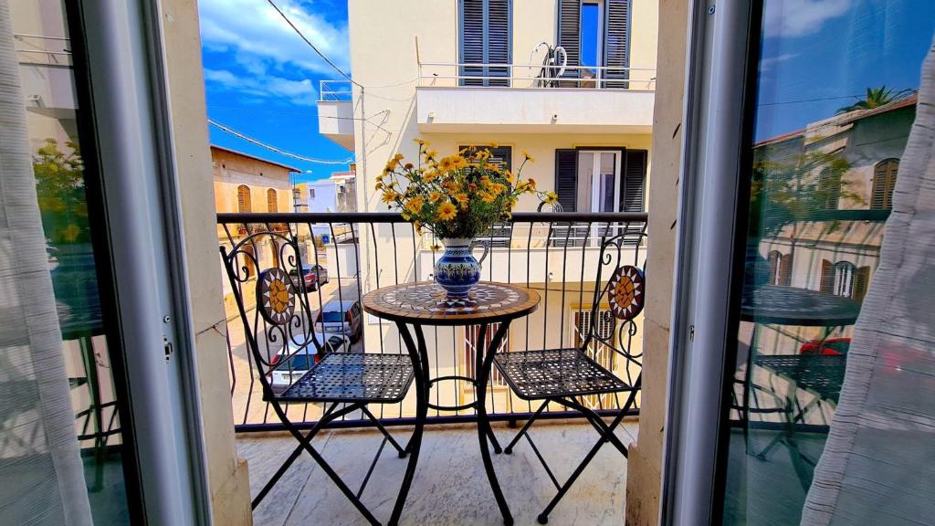 una mesa y sillas en un balcón con un jarrón de flores en Fortuna Guest House, en Siracusa