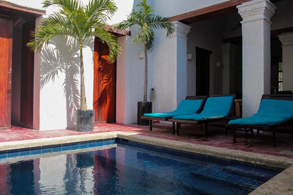 a swimming pool with two blue chairs and a palm tree at Casa Gaitana - Alma Hotels in Santa Marta