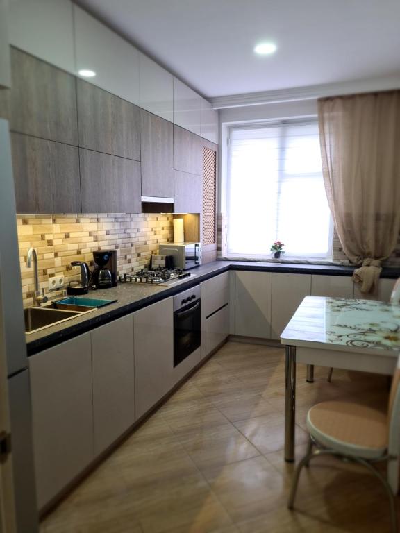 cocina con armarios blancos, mesa y ventana en New Аpartment Balti en Bălţi